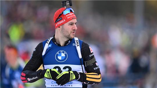 Biathlet mit rotem Stirnband, schwarzem Anzug mit gelben und roten Streifen und blauer Startnummerbei einem Wettkampf