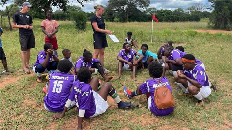 Goslarer CvD-Gymnasium erläuft 8500 Euro für „Girls in Action“ Jugendliche Fußballspieler in lila Trikots sitzen im Kreis auf einem Spielfeld, während zwei Trainer daneben stehen und eine Taktiktafel halten.