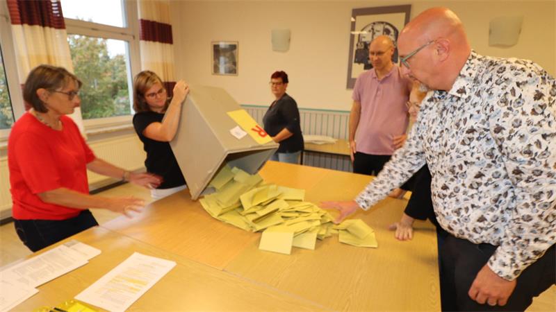 Menschen stehen um einen Tisch, auf dem eine Wahlurne entleert wird.