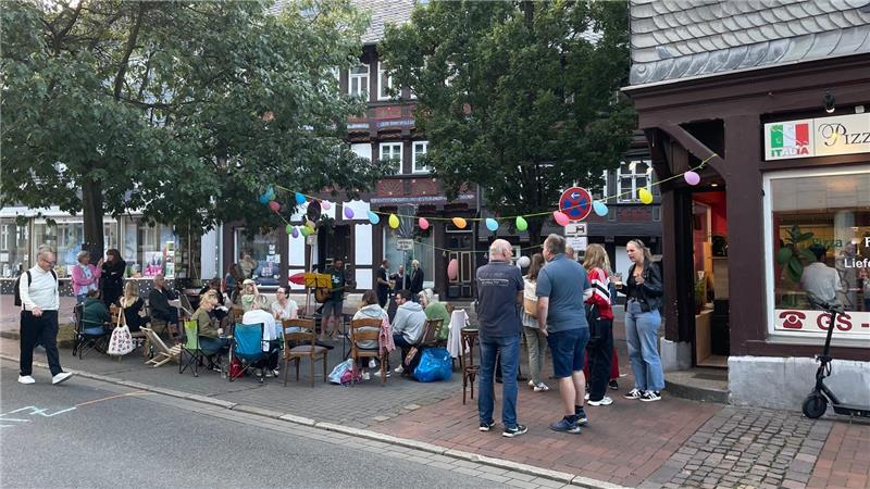 Gruppe von Menschen sitzt und steht auf einer Straße vor einem Gebäude mit Bäumen und Lichterketten