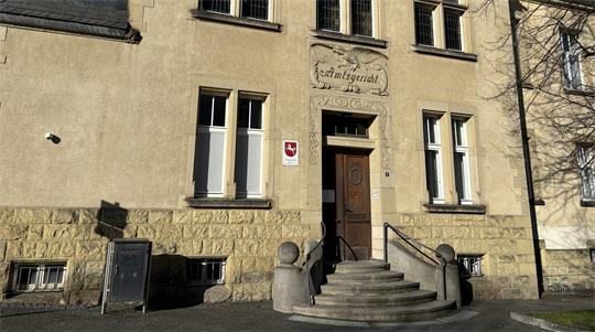 Fassade eines historischen Gebäudes mit steinerner Treppe, Holzportal und mehreren Fenstern.