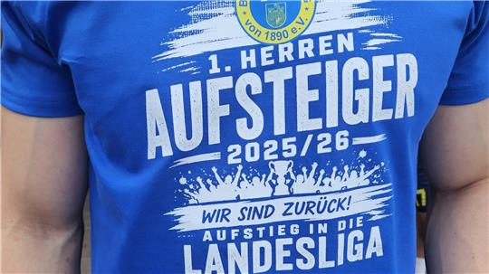 Oberkörper eines Mannes in blauem T-Shirt mit Aufdruck 'TSG Bad Harzburg von 1890 e.V. 1. Herren Aufsteiger 2025/26 Wir sind zurück Aufstieg in die Landesliga' 