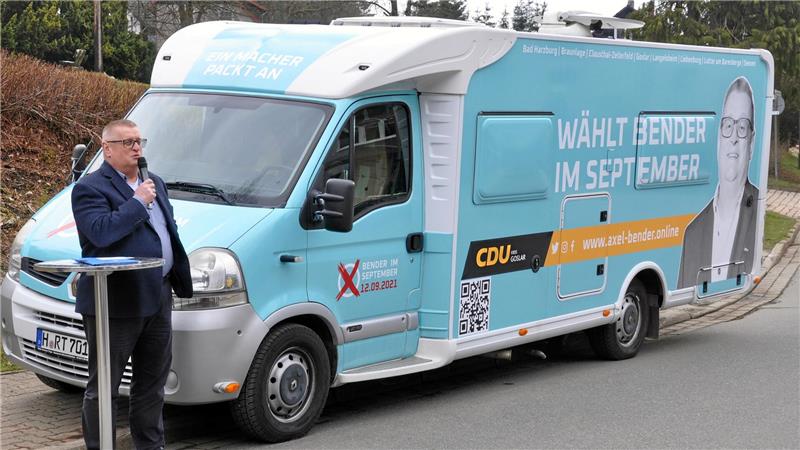 Ein Mann steht vor einem Wohnwagen und spricht in ein Mikrofon.