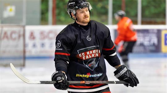 Eishockeyspieler in schwarzem Trikot mit Helm und Handschuhen hält Schläger auf dem Eis