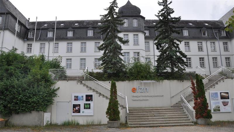 Mehrstöckiges historisches Gebäude mit Walmdach und zwei großen Tannen vor der Fassade