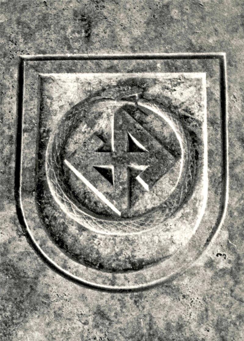 Relief mit einem Schild, darin ein Kreis mit vier spitz zulaufenden Dreiecken, die ein Kreuz bilden.