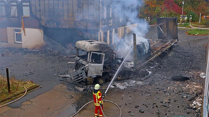 Ein Feuerwehrmann steht mit einem Löschschlauch vor einem ausgebrannten Lkw.