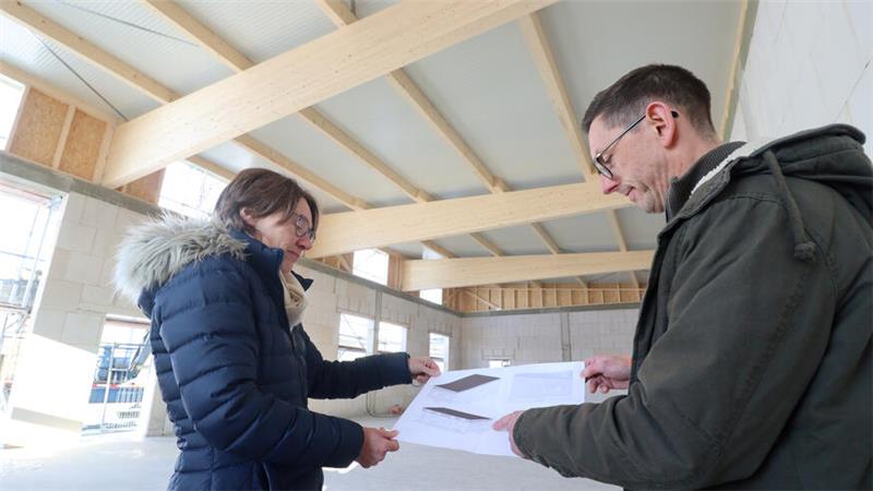 Zwei Personen begutachten in einer sich im Bau befindlichen Halle einen Plan.