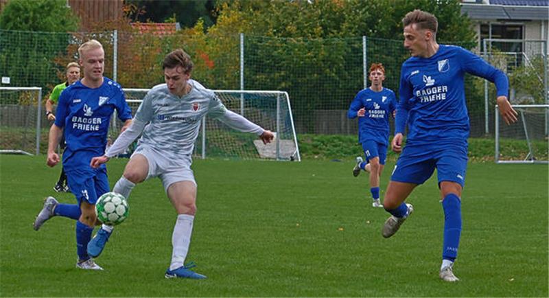 Fußballspieler in blauen und weißen Trikots kämpfen um den Ball auf einem Rasenplatz vor einem Tor und Häusern im Hintergrund