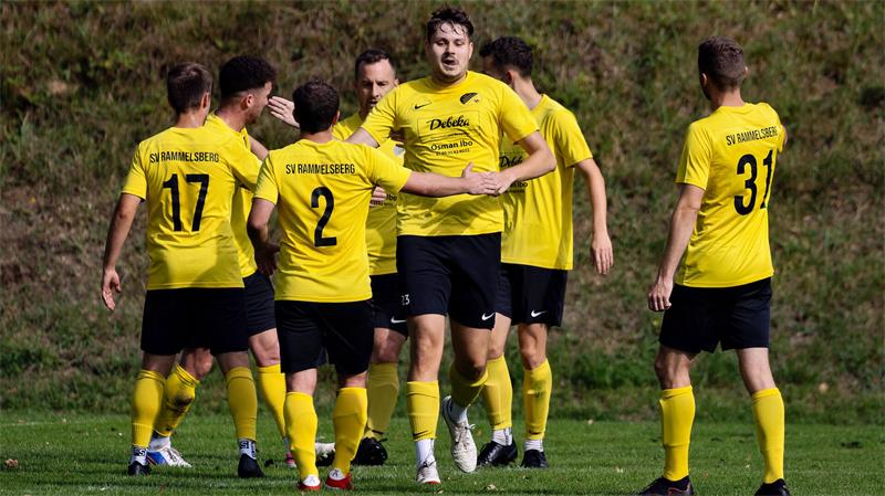 Fußballspieler in gelben Trikots mit der Aufschrift 'SV Rammelsberg' auf dem Rücken stehen auf einem Spielfeld und bejubeln ein Tor