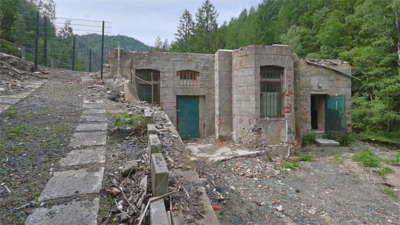 Verfallenes steinernes Gebäude mit grünen Türen in bewaldeter Berglandschaft