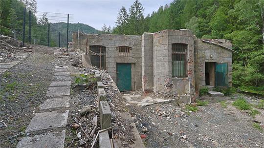 Verfallenes steinernes Gebäude mit grünen Türen in bewaldeter Berglandschaft