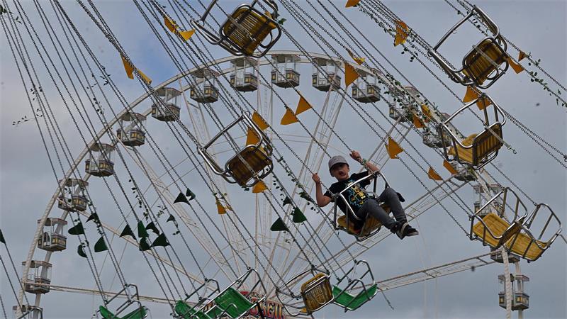 Person sitzt in einer gelben Gondel eines Kettenkarussells, das sich vor bewölktem Himmel dreht
