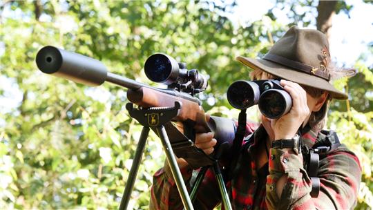 Eine Jägerin schaut neben ihrem Gewehr durch ein Fernrohr, bevor sie auf Jagd in ihrem Revier geht.