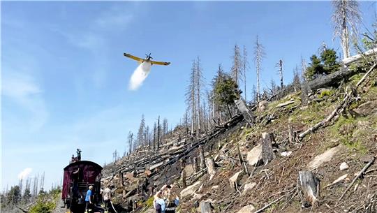 Das Löschflugzeug wirft am Königsberg am Brocken Löschwasser ab. Einsatzkräfte stehen an den Schienen.  Foto: Feuerwehr