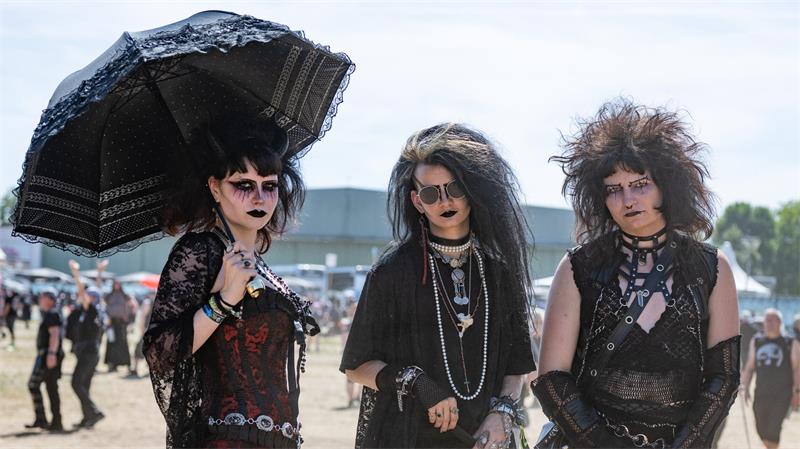 Drei Personen in schwarzer Gothic-Kleidung mit auffälligen Frisuren und Accessoires stehen im Freien, eine hält einen schwarzen Spitzenregenschirm