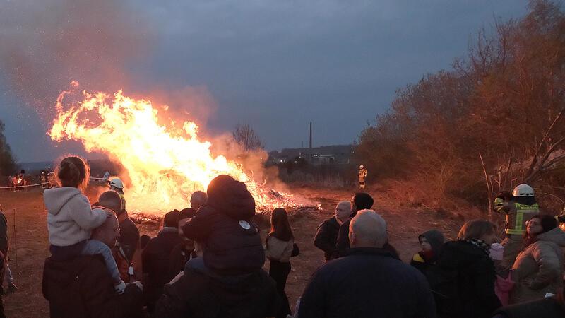 Eine Gruppe von Menschen steht bei Dämmerung vor großem Feuer im Freien.
