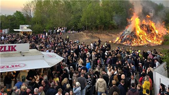 Vile Menschen schauen auf ein Osterfeuer, das licherloh brennt. 