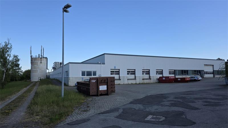 Weitläufiges Industriegebäude mit mehreren Fenstern und Containern davor unter klarem Himmel