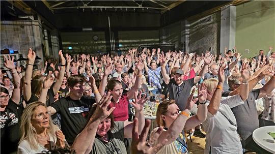 Große Menschenmenge in einer Halle mit erhobenen Armen und Händen,