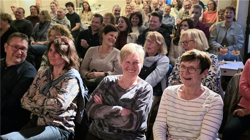Gruppe von Menschen unterschiedlichen Alters sitzt in einem Raum und blickt zur Kamera