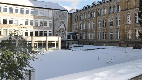 Verschneiter Innenhof mit mehreren mehrstöckigen Gebäuden im Hintergrund und einem großen Baum links im Vordergrund.