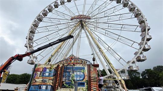 Riesenrad mit Gondeln und bemaltem Eingangsbereich vor bewölktem Himmel.