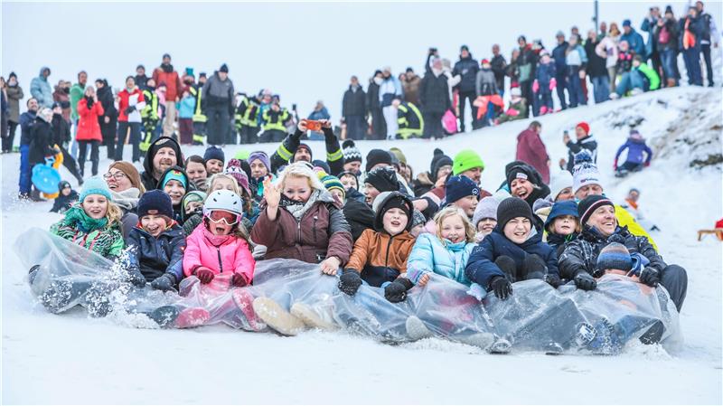 Dutzende von Menschen rutschen auf einer Plane ins Tal.