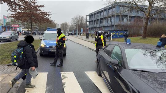 Vermumte Personen stehen auf einer Straße vor einem Schulgebäude.