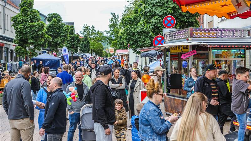 Menschenmenge auf einer belebten Straße mit Verkaufsständen und Bäumen im Hintergrund