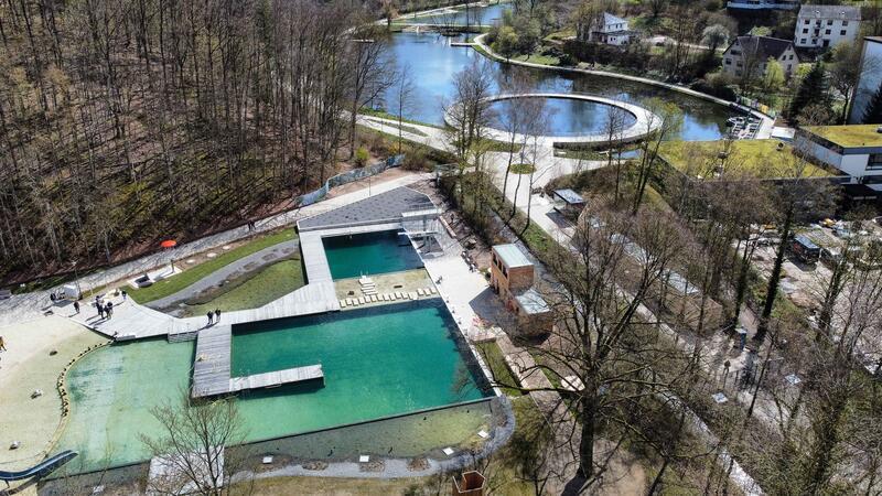 Luftaufnahme eines Schwimmbads mit mehreren Becken und umliegenden Wegen in einem bewaldeten Gebiet