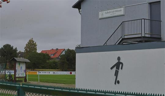 Gebäude mit Schild "Fußball-Club Othfresen" und stilisierte Figur mit Fußball an der Wand neben einem Fußballplatz