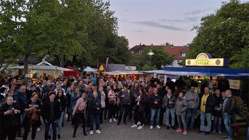 Menschenmenge auf einem Festplatz, im Hintergrund sind Bierwagen zu sehen. 