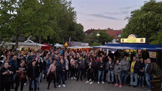 Menschenmenge auf einem Festplatz, im Hintergrund sind Bierwagen zu sehen. 