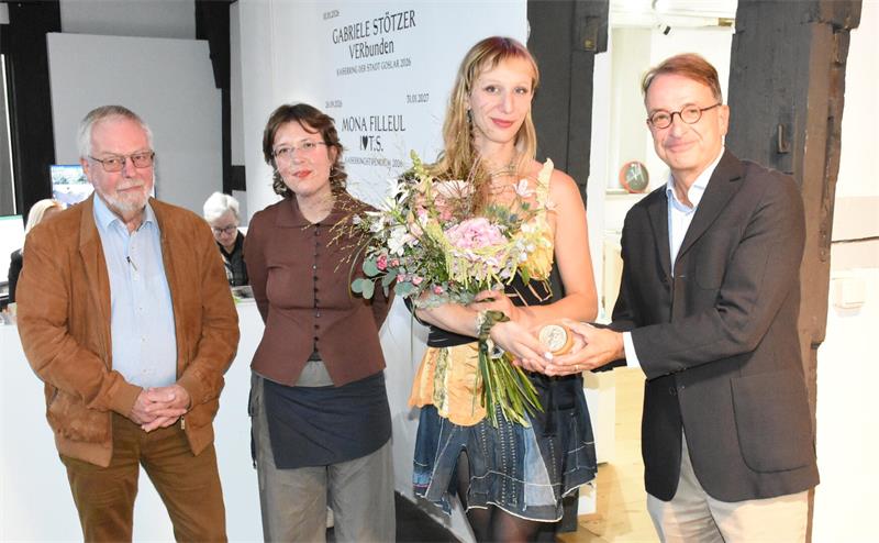 Vier Menschen stehen nebeneinander, die zweite von rechts bekommt Blumen und eine Medaille.
