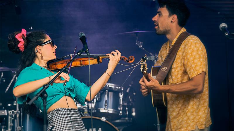 Zwei Musiker in flippigem Outfit spielen auf einer Bühne Geige und Gitarre.