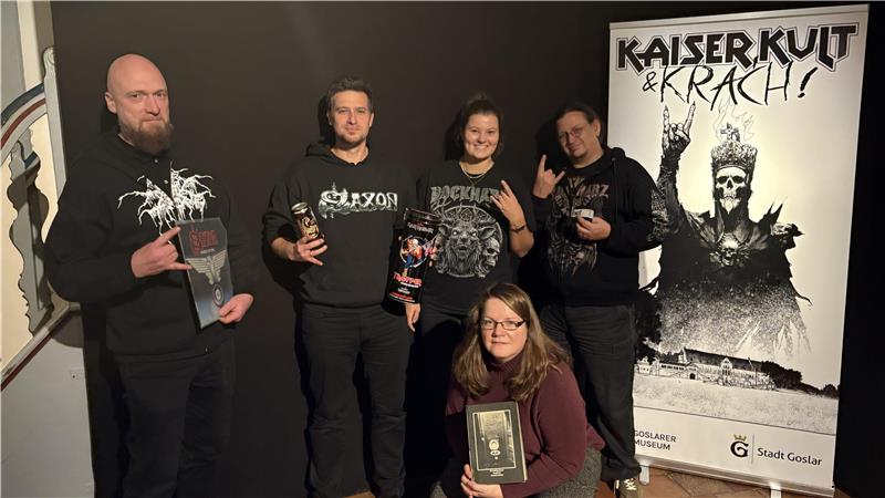 Fünf Personen in dunkler Kleidung posieren mit Pommesgabel vor einem Banner mit der Aufschrift 'KAISER KULT & KRACH!' und einer Skelettfigur mit erhobener Hand.