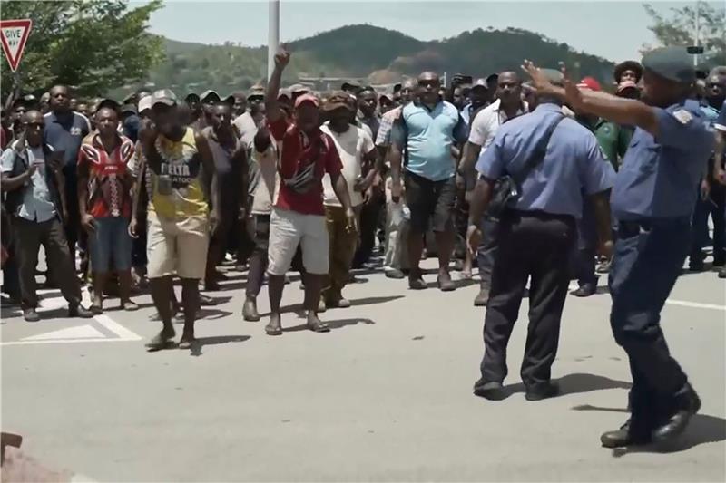 Das Videostandbild zeigt zwei Polizisten neben einer aufgebrachten Menschenmenge in Port Moresby.