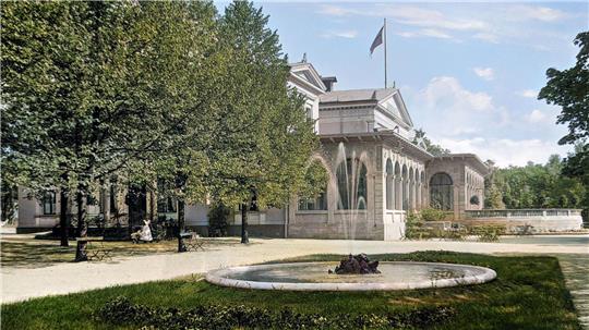 Zusehen ist ein Brunnen in einem Garten und im Hintergrund ist ein weißes Gebäude mit einer Flagge auf dem Dach.