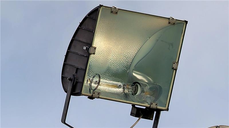 Nahaufnahme eines großen, rechteckigen Flutlichts mit Glasabdeckung und Metallrahmen vor blauem Himmel