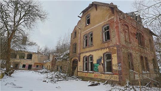 Verfallenes mehrstöckiges Backsteingebäude mit zerbrochenen Fenstern und Graffiti im verschneiten Wald