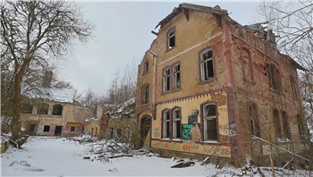 Verfallenes mehrstöckiges Backsteingebäude mit zerbrochenen Fenstern und Graffiti im verschneiten Wald