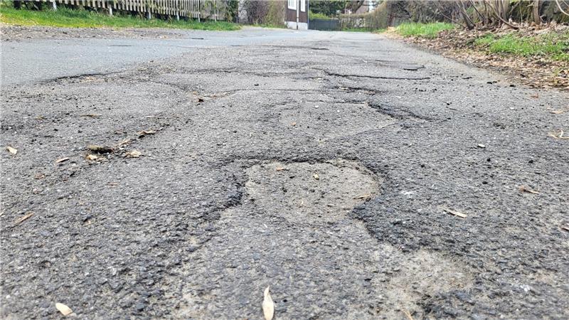 Nahaufnahme einer unebenen Asphaltstraße mit mehreren Schlaglöchern und Rissen