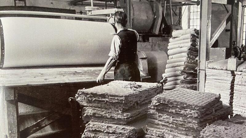 Blick in einen nahezu unbekannten Teil der Harzburger Geschichte Das historische Bild aus dem Buch zeigt, wie der Holzstoff von der Walze geschnitten und daneben lose gestapelt wird, bevor er maschinell trocken gepresst wird (ganz rechts im Bild).