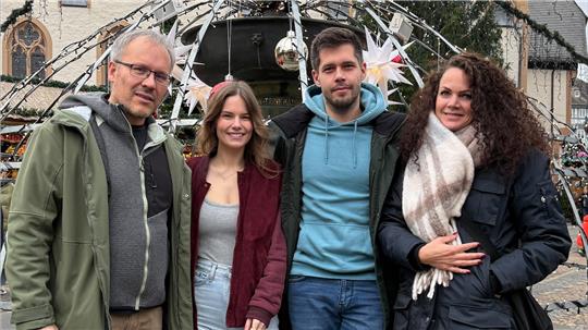 Vier Personen stehen vor dem mit Lichterketten und Weihnachtssternen geschmückten Goslarer Marktbrunnen im Freien.