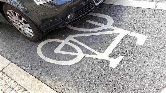 Vorderer Teil eines geparkten Autos steht auf einem Fahrrad-Piktogramm auf der Straße