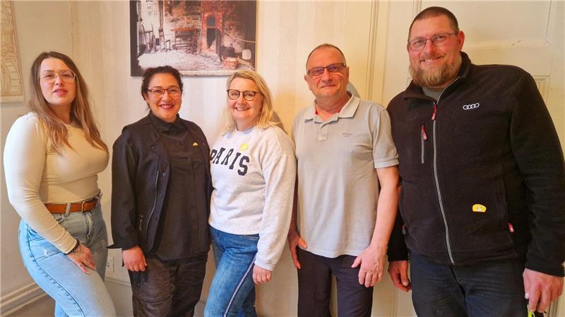 Fünf Personen stehen nebeneinander vor einer Wand mit einem gerahmten Bild