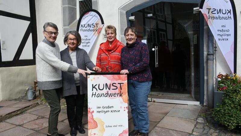 Vier Frauen stehen vor einem Hauseingang, der von Beachflags eingerahmt wird, hinter einem Aufsteller.