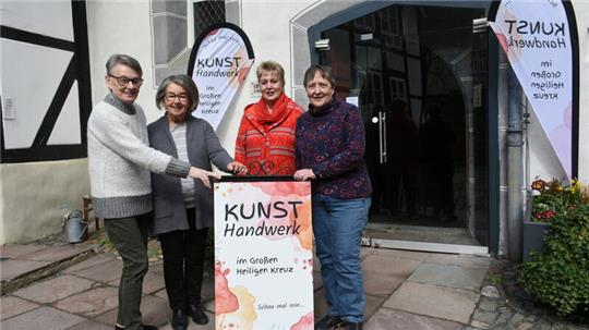 Vier Frauen stehen vor einem Hauseingang, der von Beachflags eingerahmt wird, hinter einem Aufsteller.