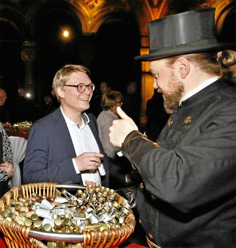Herr des Goslarer Geldes: Dr. Pascal Bothe (CDU) mag Zahlenarbeit Zwei Männer unterhalten sich, einer ist Schornsteinfeger, trägt einen Zylinderhut und gibt ein Daumen-hoch-Zeichen, vor ihnen ein großer Korb mit kleinen Fläschchen